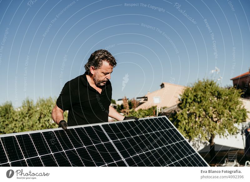 mature Technician man holding solar panels on house roof for self consumption energy. Renewable energies and green energy concept technician photovoltaic tools