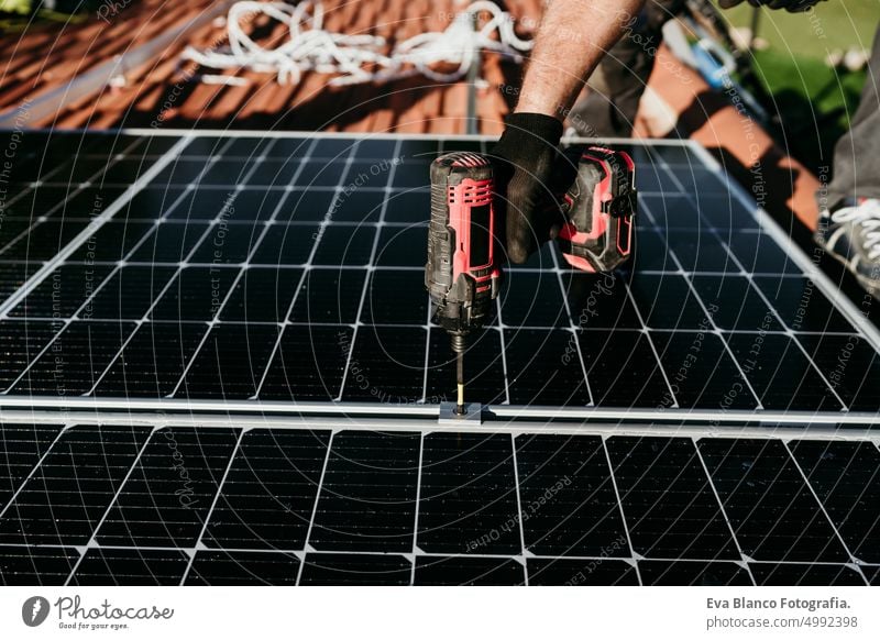 hand of mature Technician man assembling solar panels with drill on house roof for self consumption energy. Renewable energies and green energy concept