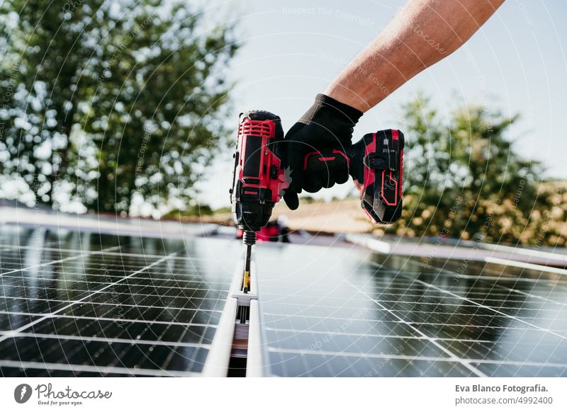 close up hand of mature Technician man assembling solar panels with drill on house roof for self consumption energy. Renewable energies and green energy concept