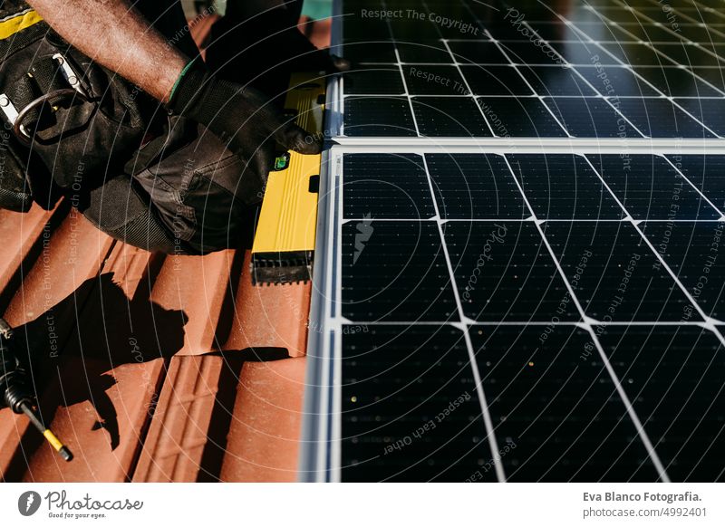 close up hands of mature Technician man using level on solar panels on house roof for self consumption energy. Renewable energies and green energy concept drill