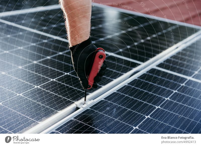 mature Technician man assembling solar panels with tool on house roof for self consumption energy. Renewable energies concept green energy technician