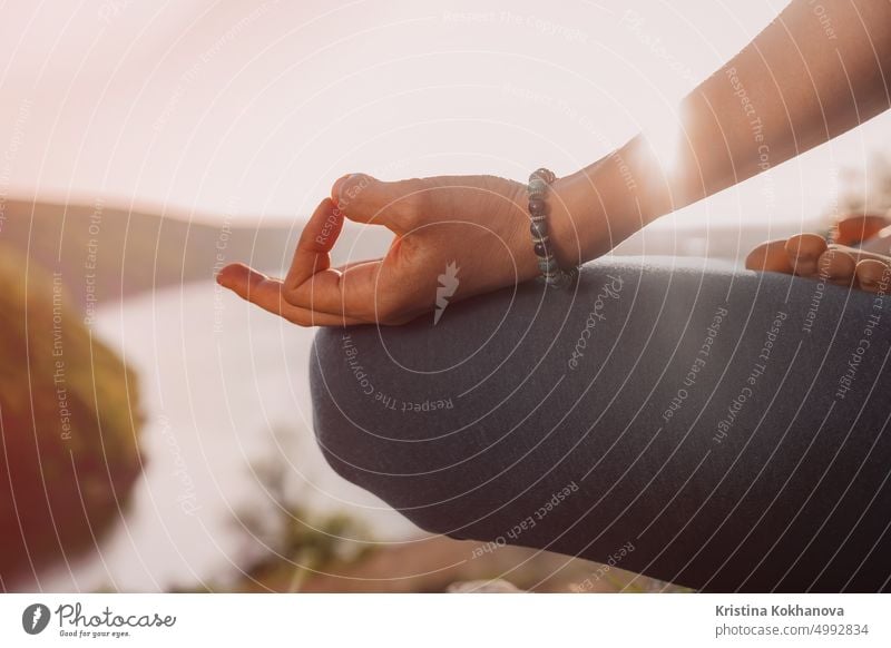 Healthy woman sitting in lotus pose and meditating on high cliff above river. Calm yoga concept, zen, relaxation, practice on nature background. female