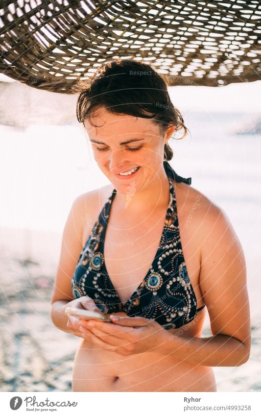 Young Caucasian Lady Woman Use Smartphone Under Beach Umbrella On Sunset. Vacation On Sea Ocean active lifestyle attractive authentic beach beautiful beauty