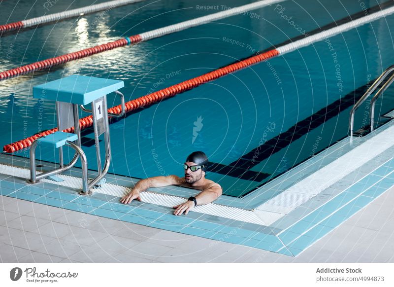 Swimmer in goggles leaning on poolside swimmer lean on hand masculine man portrait athlete sport macho tired accessory sportsman glad swimming modern