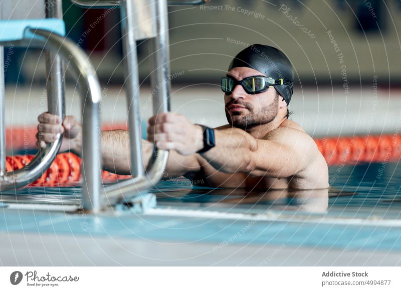 Swimmer in goggles and cap exercising in pool athlete sport workout stretch swimming exercise warm up man sportsman training block outstretch pure water number