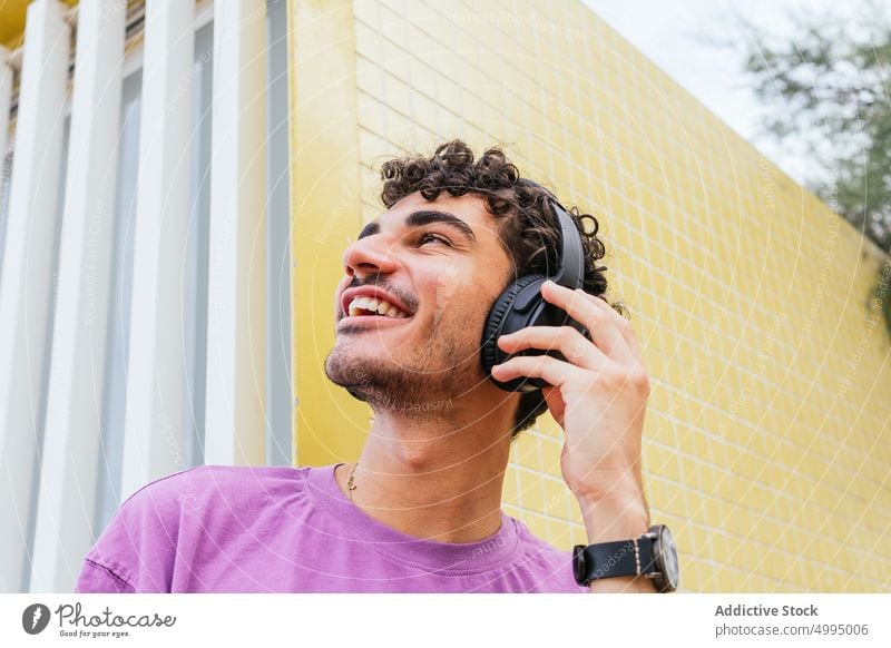 Hispanic meloman listening to music on beach adjust headphones enjoy smile weekend male hispanic ethnic young wall tile street summer song sound optimist bright