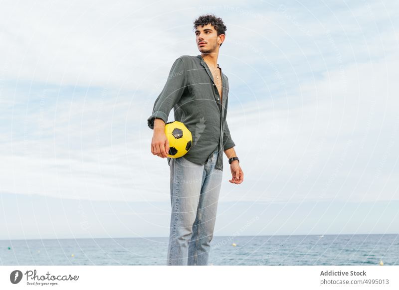 Hispanic man holding ball near sea beach kick trick summer weekend football male hispanic ethnic young activity seaside daytime casual recreation skill water