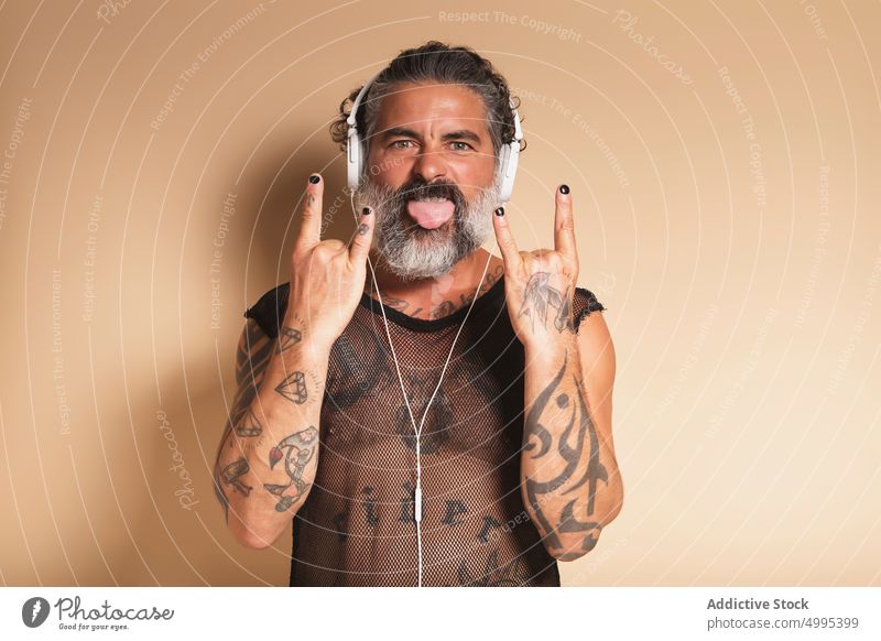 Bearded man showing rock gesture and listening to music rocker rebel tongue out rock and roll horn male mature middle finger gray beard headphones grimace