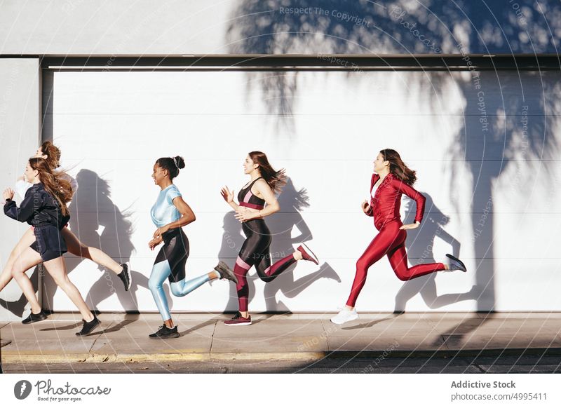 Sporty young diverse female friends running on city street women training workout positive sport together athlete exercise wellbeing wellness fitness