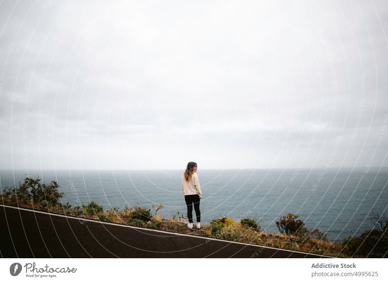 Woman standing on road near the sea woman traveler cloudy sky weekend trip asphalt la palma canary islands walk spain casual overcast route shore path tourist