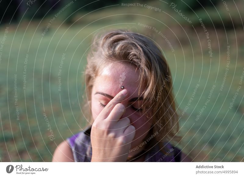 Tranquil woman touching forehead while meditating in nature with closed eyes meditate eyes closed shaman touch forehead harmony stress relief yoga peaceful