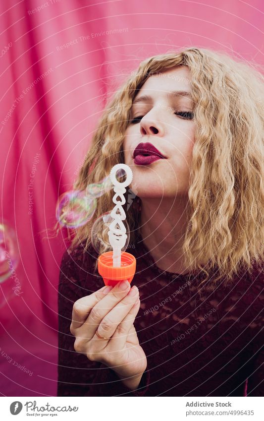 Young woman blowing soap bubbles style blond wavy hair carefree trendy studio model female hairstyle playful lady childish individuality personality feminine