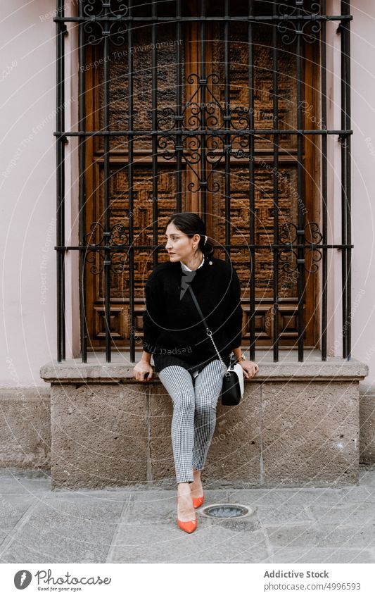 Hispanic woman sitting near wooden door on street calm city style gorgeous feminine building personality alone dreamy female young ethnic hispanic brunette