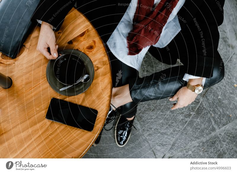 Crop stylish lady sitting in street cafe with coffee cup and smartphone woman coffee break style beverage aromatic trendy table female white shirt coat