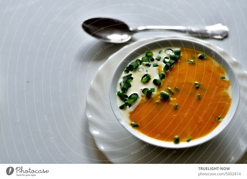 Pumpkin soup with a little cream and spring onion greens chopped in white bowl on white plate and a soup spoon Soup Orange Cream White Chives Green Warmth