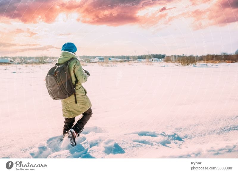 Young Woman Tourist Lady Photograph Taking Pictures Of Snowy Landscape In Sunny Winter Day. Active Lifestyle With Backpack And Camera. Altered Sunset Sky