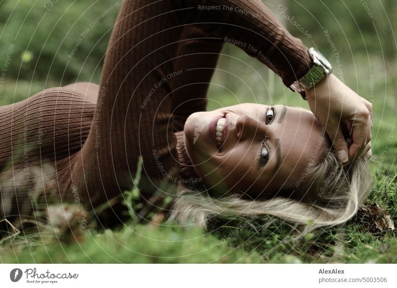 Young blonde woman with dimples lies on the moss in the forest and smiles at the camera from the side Young woman Woman Blonde Feminine pretty fortunate