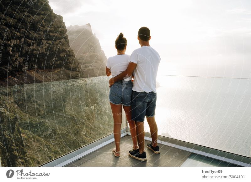 Young couple on a viewpoint against volcanic cliffs and the ocean love honeymoon young sunset caucasian copy space rocks canary islands spain sea black sky trip