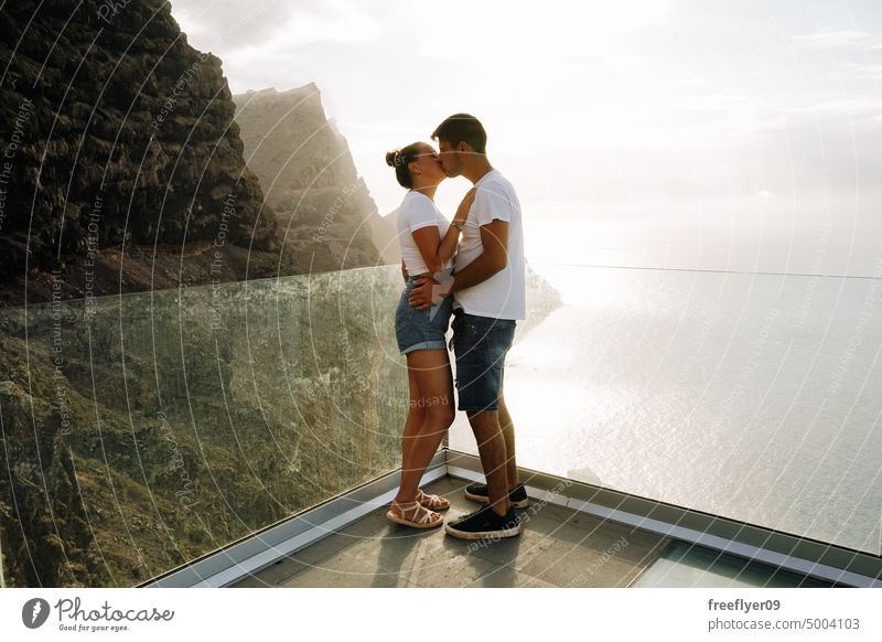 Young couple on a viewpoint against volcanic cliffs and the ocean love honeymoon young sunset caucasian copy space rocks canary islands spain sea black sky trip