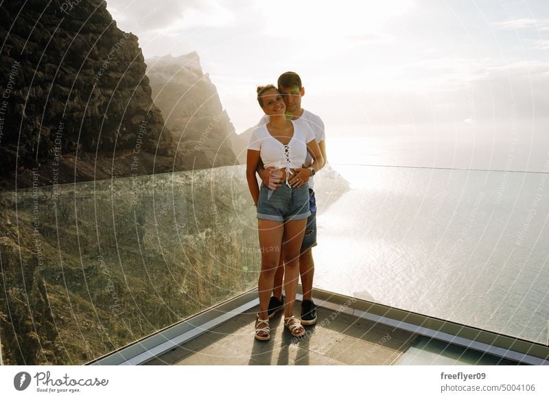 Young couple on a viewpoint against volcanic cliffs and the ocean love honeymoon young sunset caucasian copy space rocks canary islands spain sea black sky trip