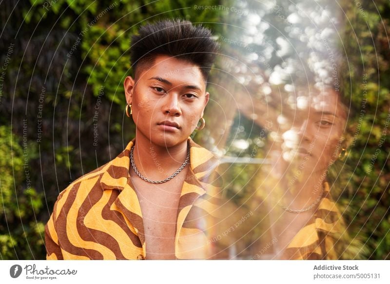 Handsome non binary guy in trendy shirt against bushes man confident portrait lgbt queer complexion individuality face natural beauty skin nature acne cosmetic