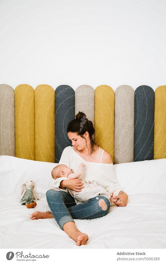 Happy mother feeding tranquil baby while relaxing on bed together at home infant kid parent eat mom harmony child comfort care newborn bedroom love milk