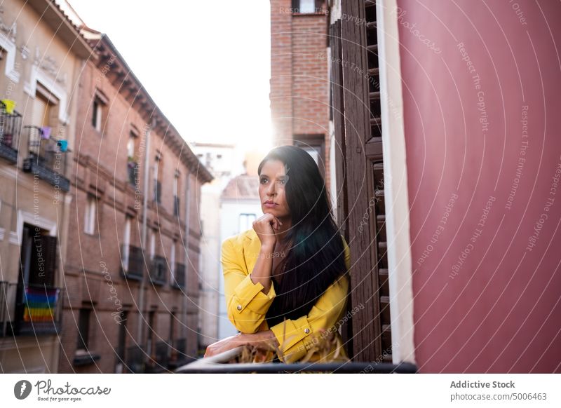 Calm young woman standing on balcony in city calm tranquil urban town elegant brunette sensual street female trendy rest sunny charming positive attractive