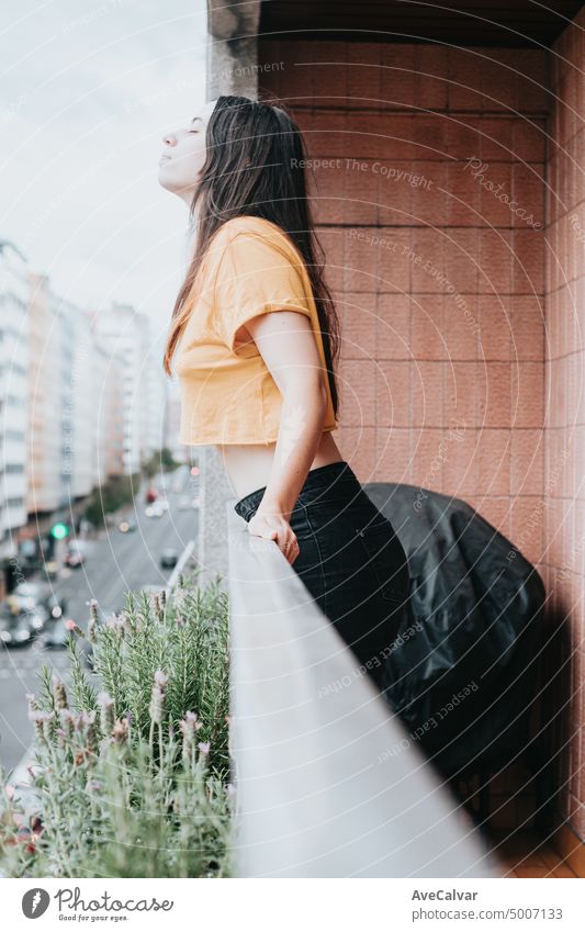 Beautiful caucasian woman breathing fresh air on the balcony of the apartment at the city during a free day of work. Stresfull life style at the urban city. Woman relaxing on balcony