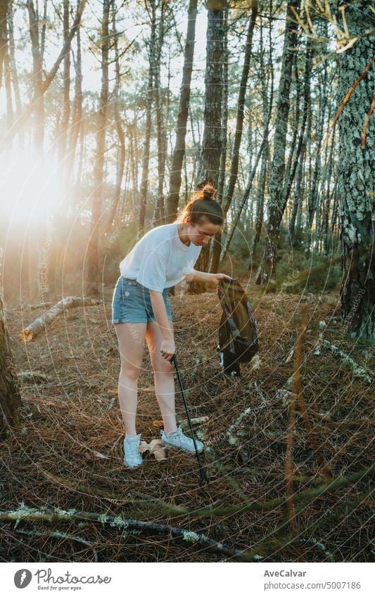 Photo of side of girl picking up garbage in bag on the forest during a sunset.Environmental garbage pollution.Nature cleaning, volunteer ecology green concept.