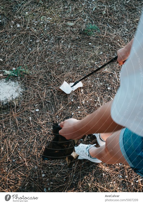 A young woman collects abandoned garbage in a black bag in the forest. Plastic pollution and environmental protection.Problem of bed ecology and environmental pollution with long-decomposing waste