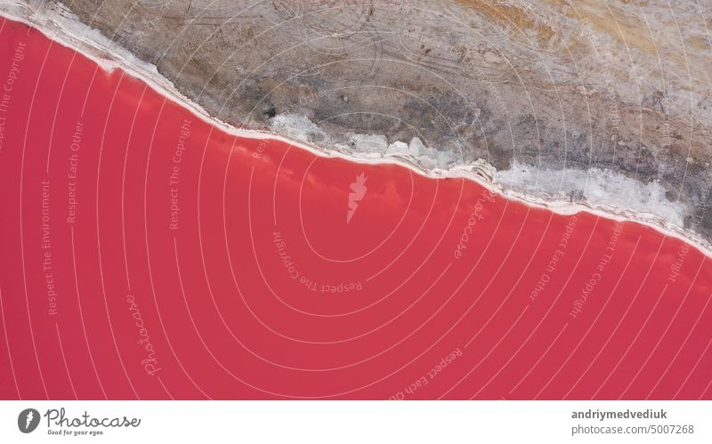 Flying over a pink salt lake. Salt production facilities saline evaporation pond fields in the salty lake. Dunaliella salina impart a red, pink water in mineral lake with dry cristallized salty coast.