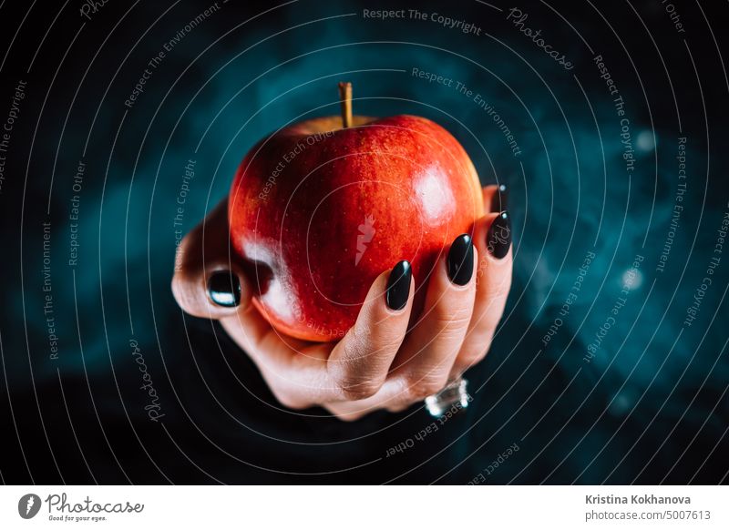 Woman as witch offers red apple - symbol of toxic proposal, lure. Fairytale, white snow, wizard concept. Halloween celebration, cosplay. Smoke, mist background.