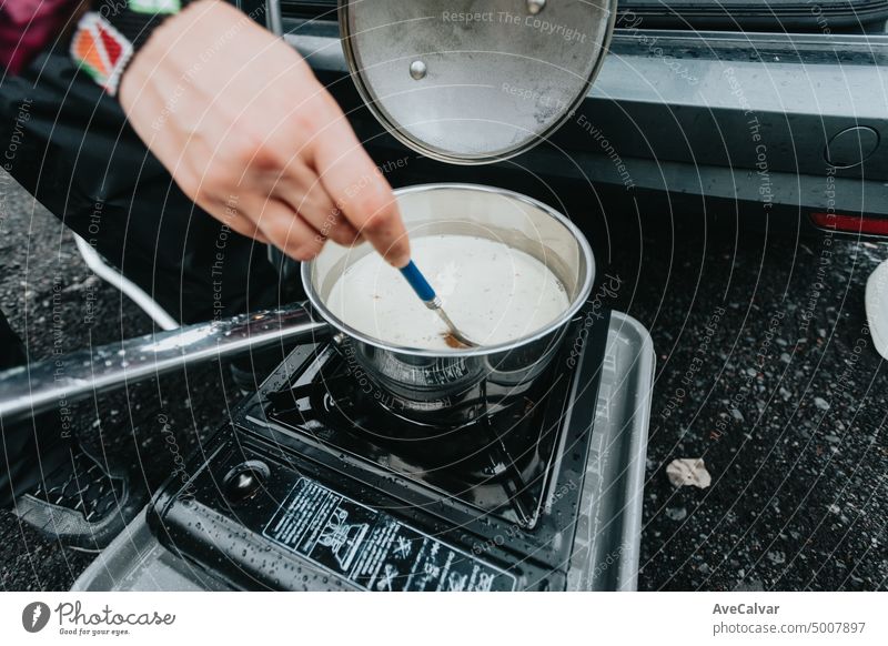 Unrecognizable woman cooking in camping gas during a rainy day.Vanlife lifestyle for urban travellers. cinematic scandinavian landscape. Travel on epic road trip through mountains.