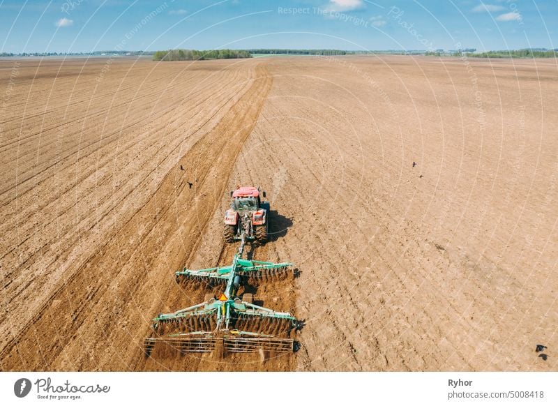 Aerial View. Tractor Plowing Field In Spring Season. Beginning Of Agricultural Spring Season. Cultivator Pulled By A Tractor In Countryside Rural Field Landscape