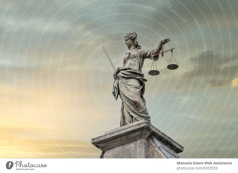 A statue of Justice, the goddess of justice, with a sword and scales on a pedestal in front of a scenic sunset Lady Justice Statue Sword Scale Balance Law fair