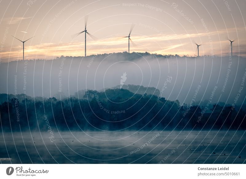 Five wind turbines above foggy lake at sunrise. Pinwheel wind power windmills Electricity Wind energy plant Renewable energy Energy industry Eco-friendly