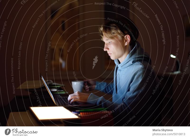 Concentrated teenager studying late night at home office with laptop and tablet. student online university internet self-employed work learn workplace