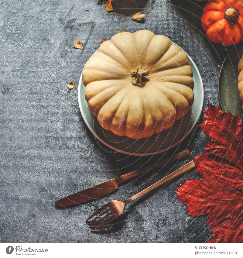 Table setting with pumpkin on plate with cutlery  and autumn leaves on dark rustic background, top view table setting fall food harvest squash thanksgiving