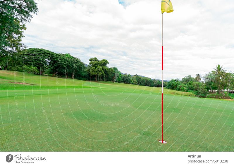 Golf course with green turf landscape. Green grass field with yellow golf flag pole. Golf course at hotel or resort. Landscape of golf course with blue sky and green trees. Green sports field.