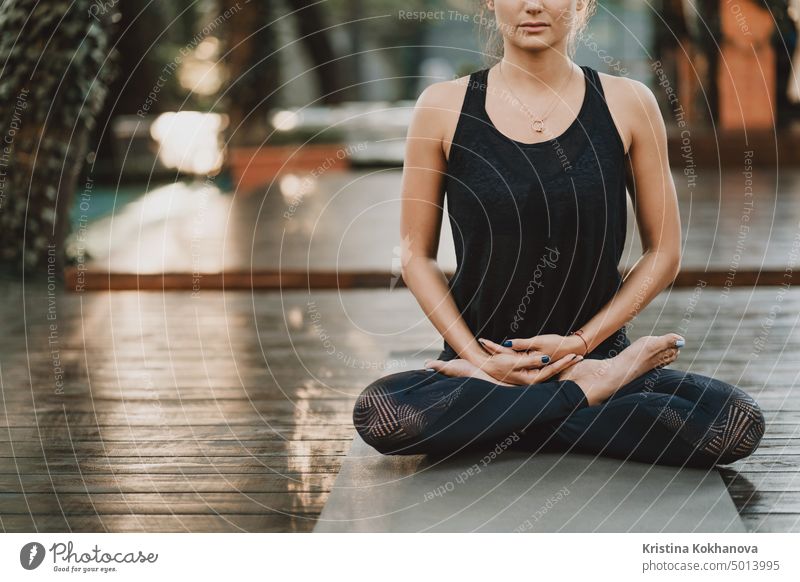 Concentrated girl sitting in lotus pose and meditating or praying. Young woman practicing yoga alone on wooden deck in tropical island. nature