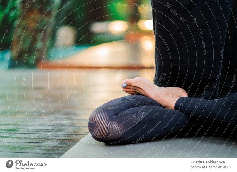 Copy space. Close up of leg in lotus pose. Girl meditating or praying. Young woman practicing yoga alone on wooden deck in tropical island. nature