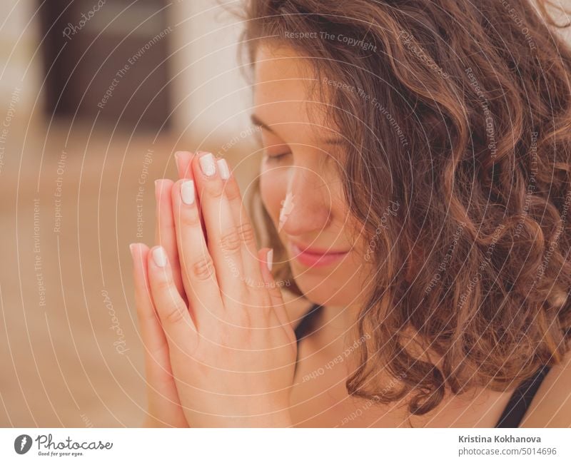 Young beautiful woman with short curly hair meditating in light fitness studio. Hands in namaste. Pray, gratitude, yoga, love God concept. female girl young