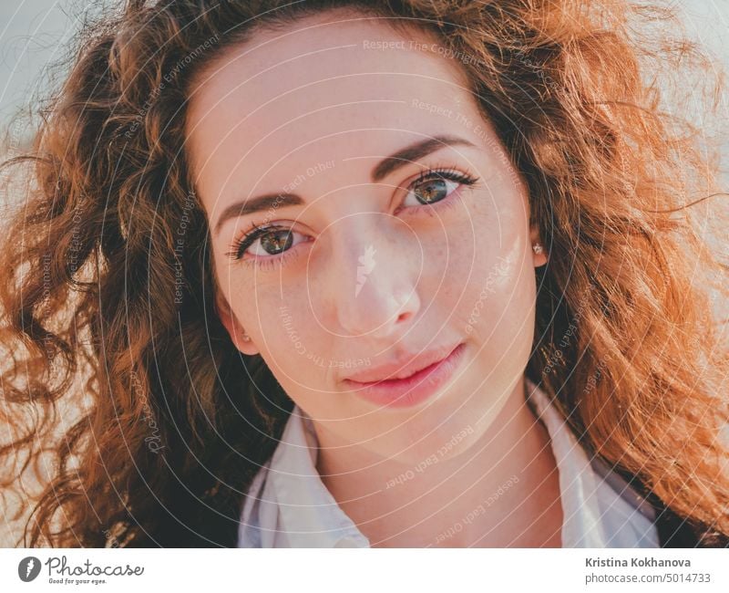 Beautiful girl with curly long hair towards the camera on sunny spring sea beach. Young stylish business woman in fashion black coat and white shirt near ocean.