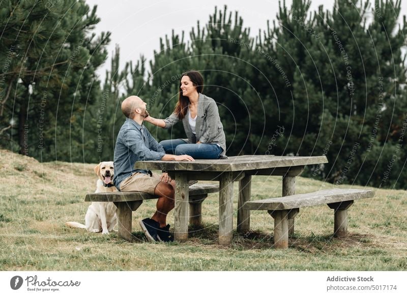 Happy owners sitting with dog on table in park couple hugging fun happy pet nature green grass animal labrador retriever joyful together friendship