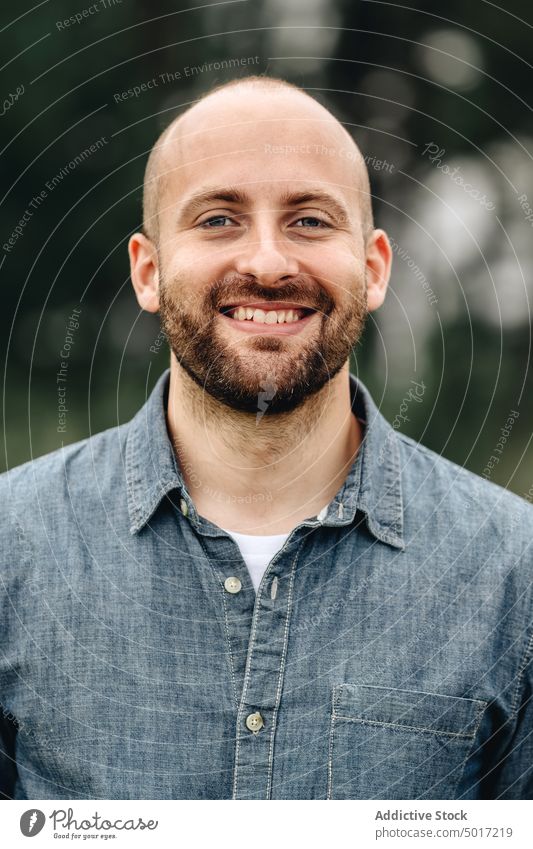 Smart bearded man in denim shirt looking at camera handsome park stylish human face portrait male young relax adult calm day nature bald confident model