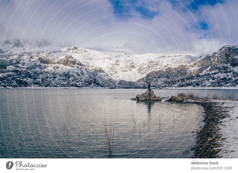 Man near paddle board on shore near water and mountains on coast man stone resting tourist surface hill sup snow sitting winter picturesque view nature travel