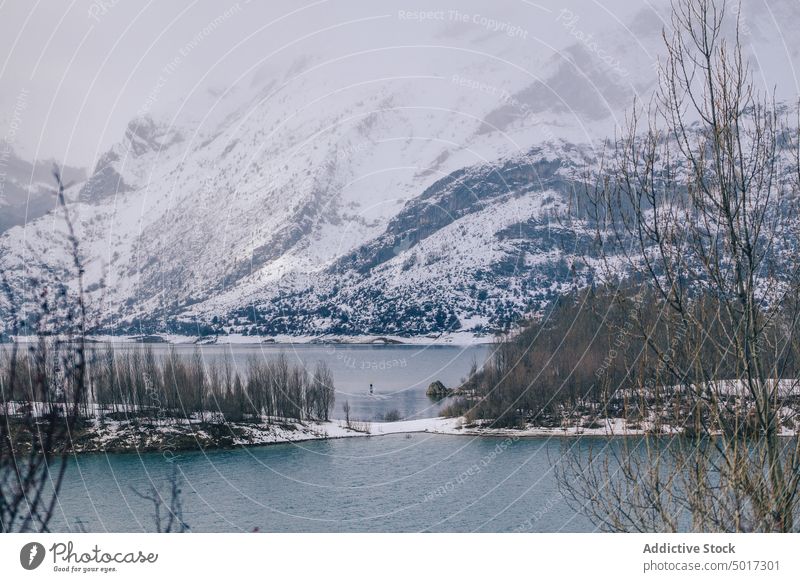 Man on paddle board between water and mountains on coast man floating tourist surface hill sup snow shore winter picturesque view stone nature travel landscape