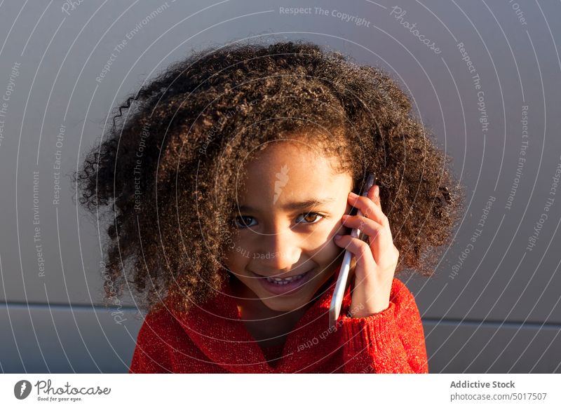 Smiling cute black girl on street using smartphone sunshine smiling cheerful child step sunny day african american happy positive walk city town hairdo