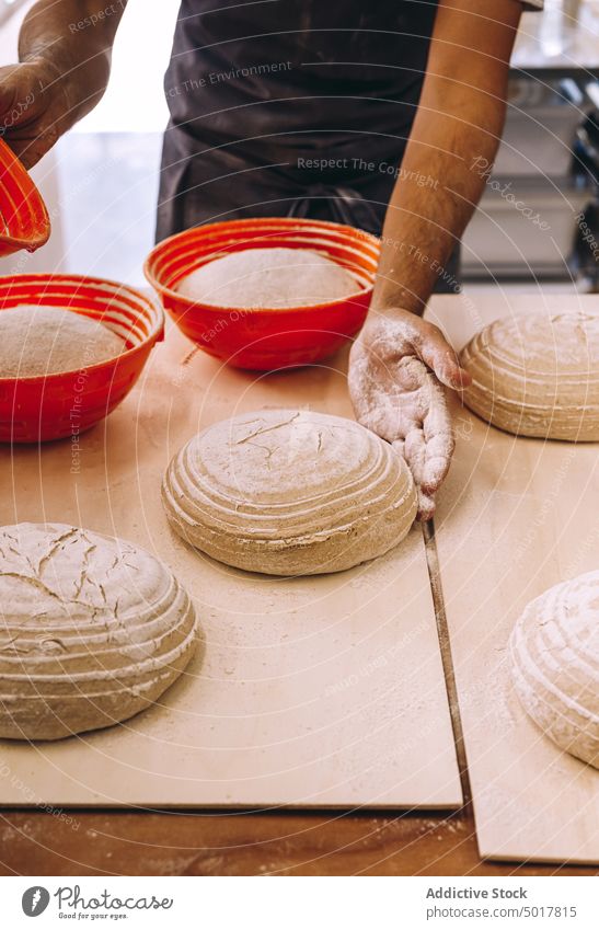 Crop male cook shaping dough with proofing basket prepare man baker bakery raw bread shape apron wooden table manufacture process production kitchen food fresh