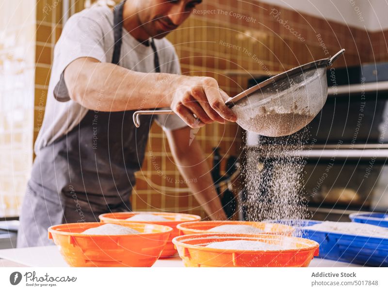 Male baker sprinkling flour on dough sprinkle man ethnic cook process scatter bread prepare male apron raw bakery food kitchen chef cuisine fresh culinary